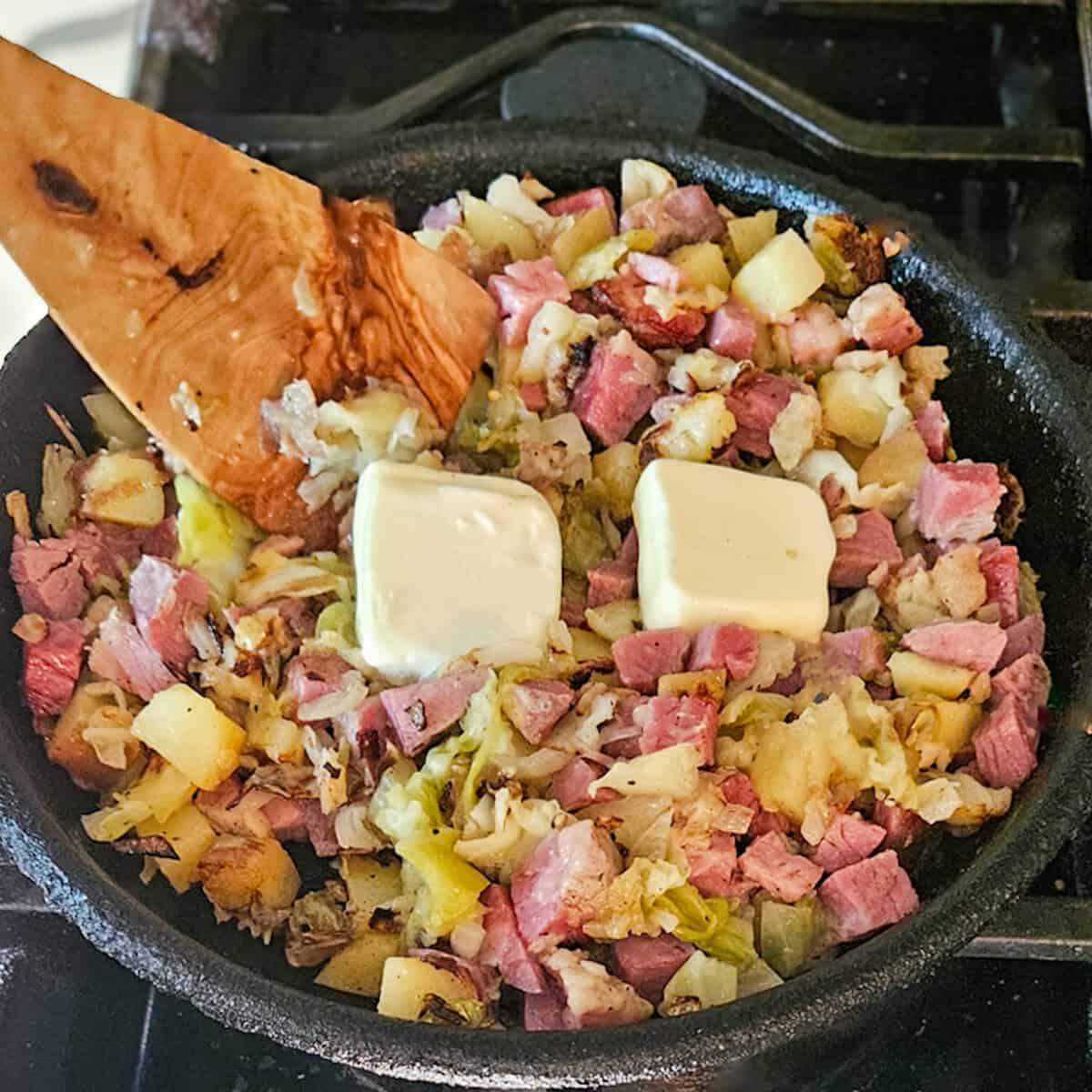 Adding butter to a skillet containing corned beef hash.