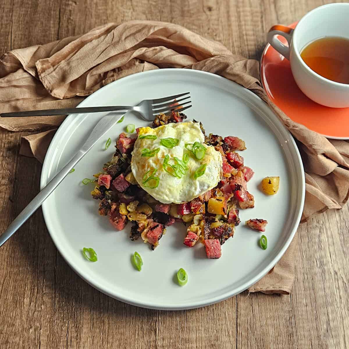 Hearty breakfast with fried egg on corned beef hash, served with tea.