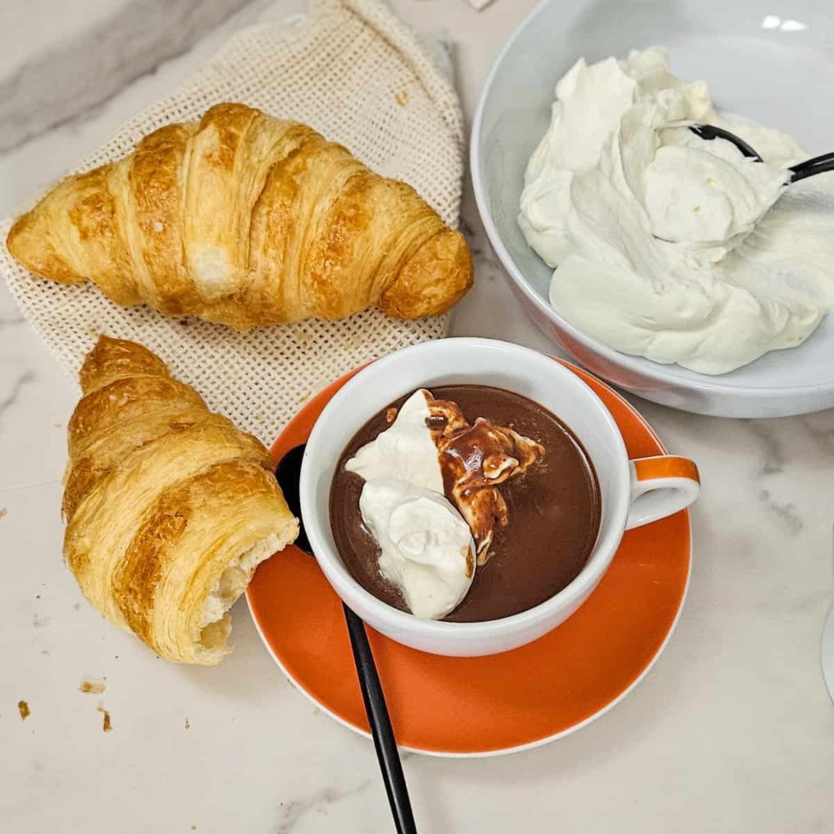 Delicious croissants served with rich hot chocolate and whipped cream for a tasty treat.
