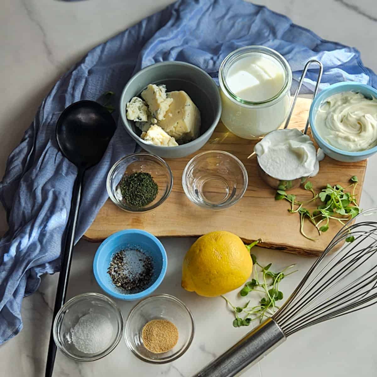 The ingredients for creamy blue cheese dressing measured out on a wooden board.