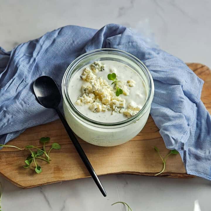 Delicious creamy blue cheese dressing garnished with herbs on a wooden board.