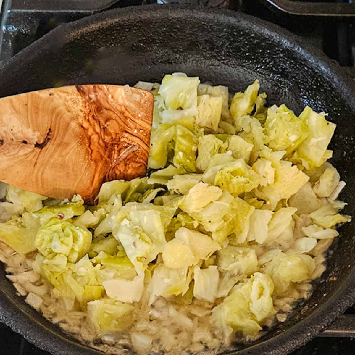 Stirring cabbage in a skillet with a wooden spatula.