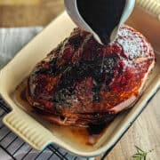 Pouring brown sugar balsamic glaze over the top of a ham in a baking dish.