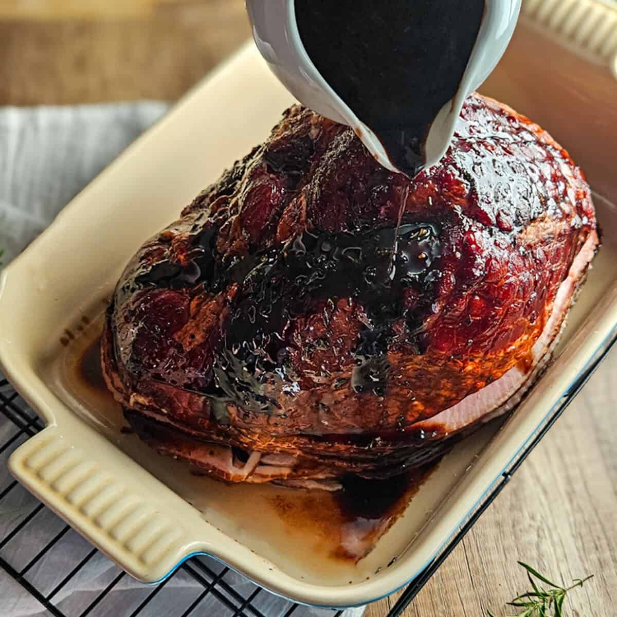 Pouring brown sugar balsamic glaze over the top of a ham in a baking dish.