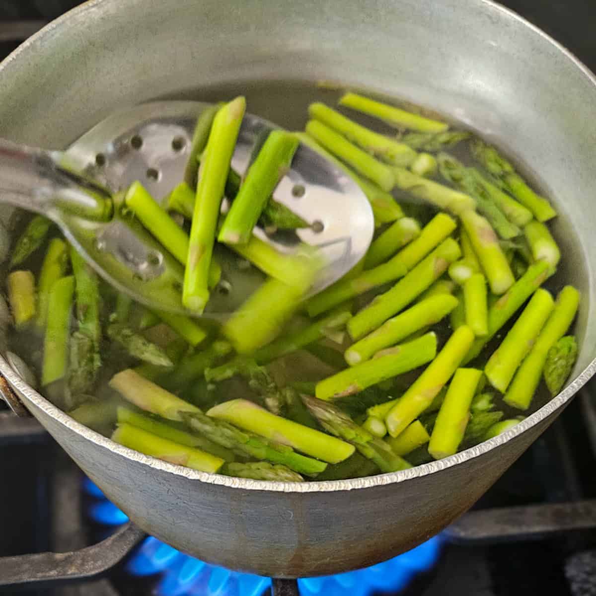 Cooking asparagus in a pot of boiling water with a slotted spoon.