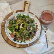 Pea and asparagus salad on a plate with a fork and spoon and a jar of blueberry balsamic dressing along side.