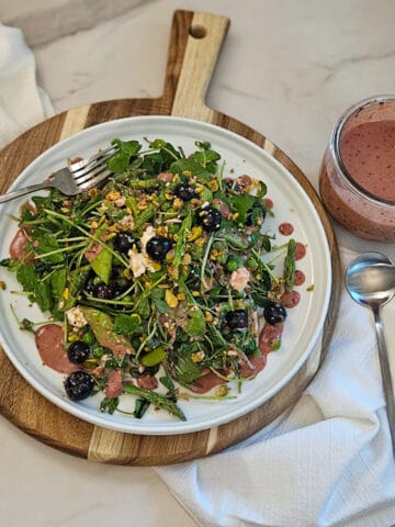 Pea and asparagus salad on a plate with a fork and spoon and a jar of blueberry balsamic dressing along side.