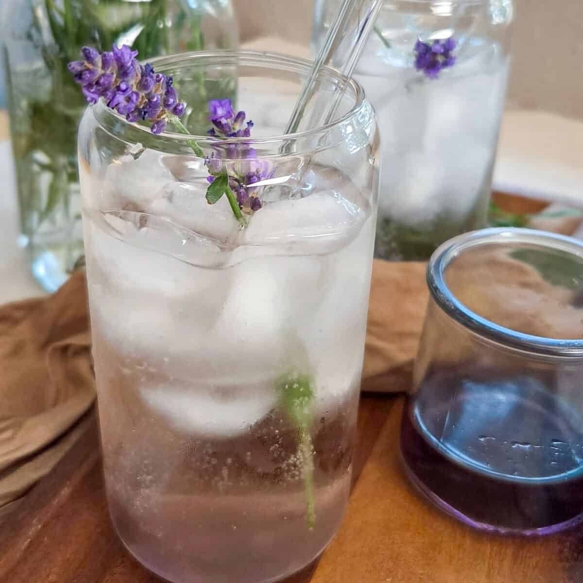 A closeup of a Lavender Rose` Spritz in a glass with ice, lavender flowers, and a straw.