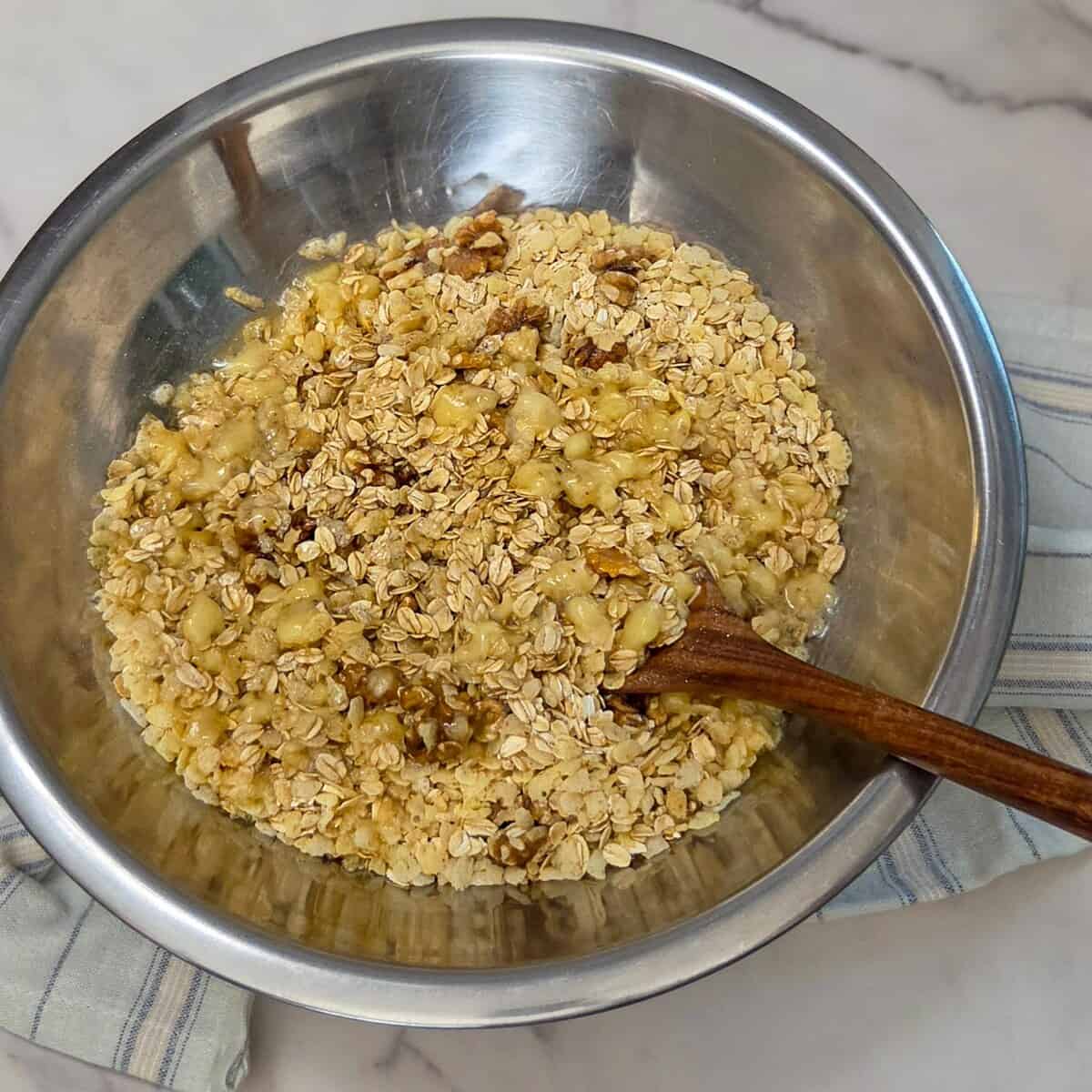 Mixing together the oat mixture with the banana mixture ina large bowl with a spoon for the banana walnut granola.
