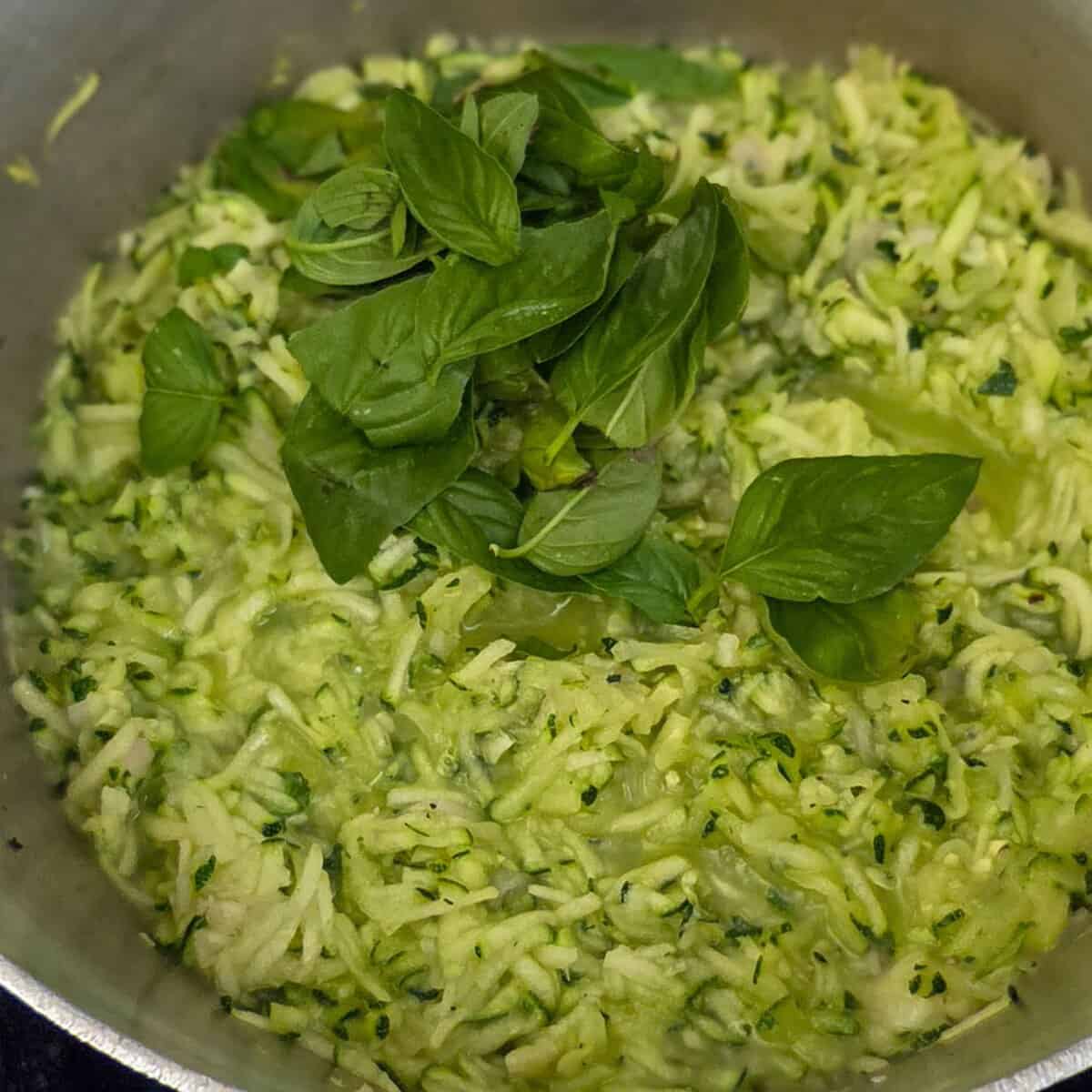 Cooking shredded zucchini and basil leaves in a saucepan.