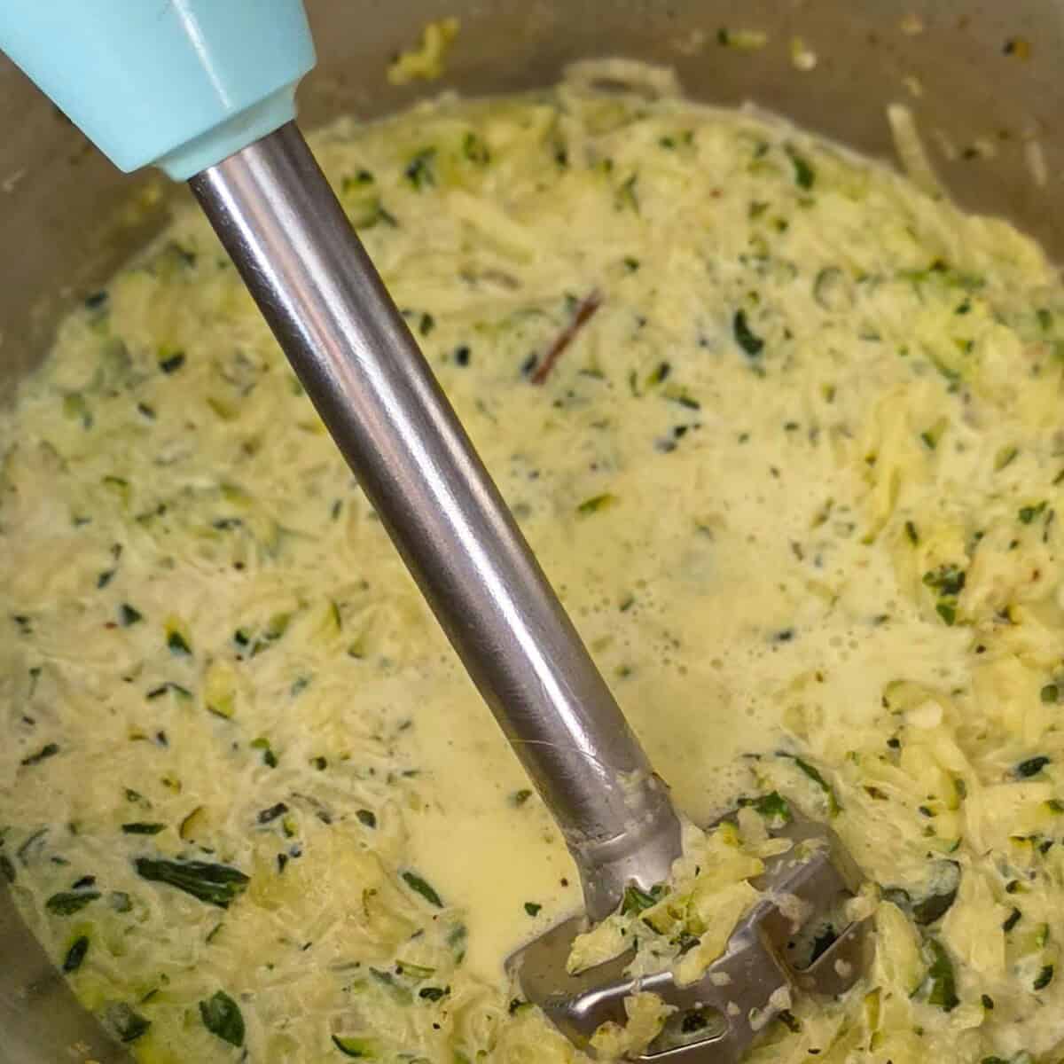 Using an immersion blender to puree the creamy zucchini alfredo sauce.