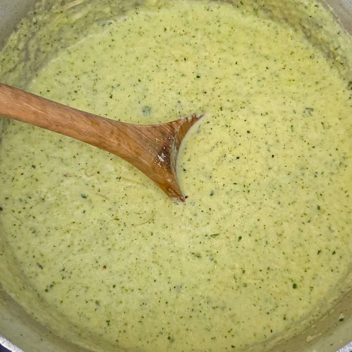 Creamy zucchini alfredo sauce in a saucepan with a wooden spoon.
