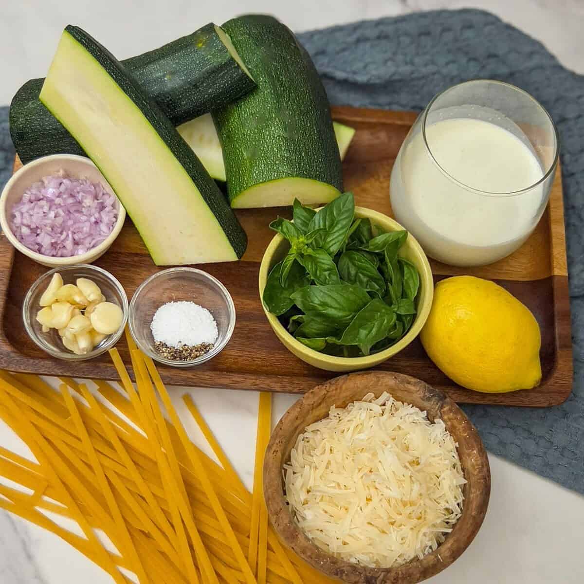 The ingredients for making creamy zucchini alfredo pasta measured into bowls.