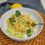 Creamy zucchini pasta with basil leaves, a fork, and a lemon in the background.