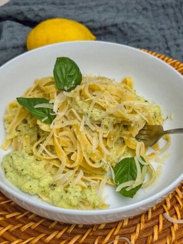 Creamy zucchini pasta with basil leaves, a fork, and a lemon in the background.
